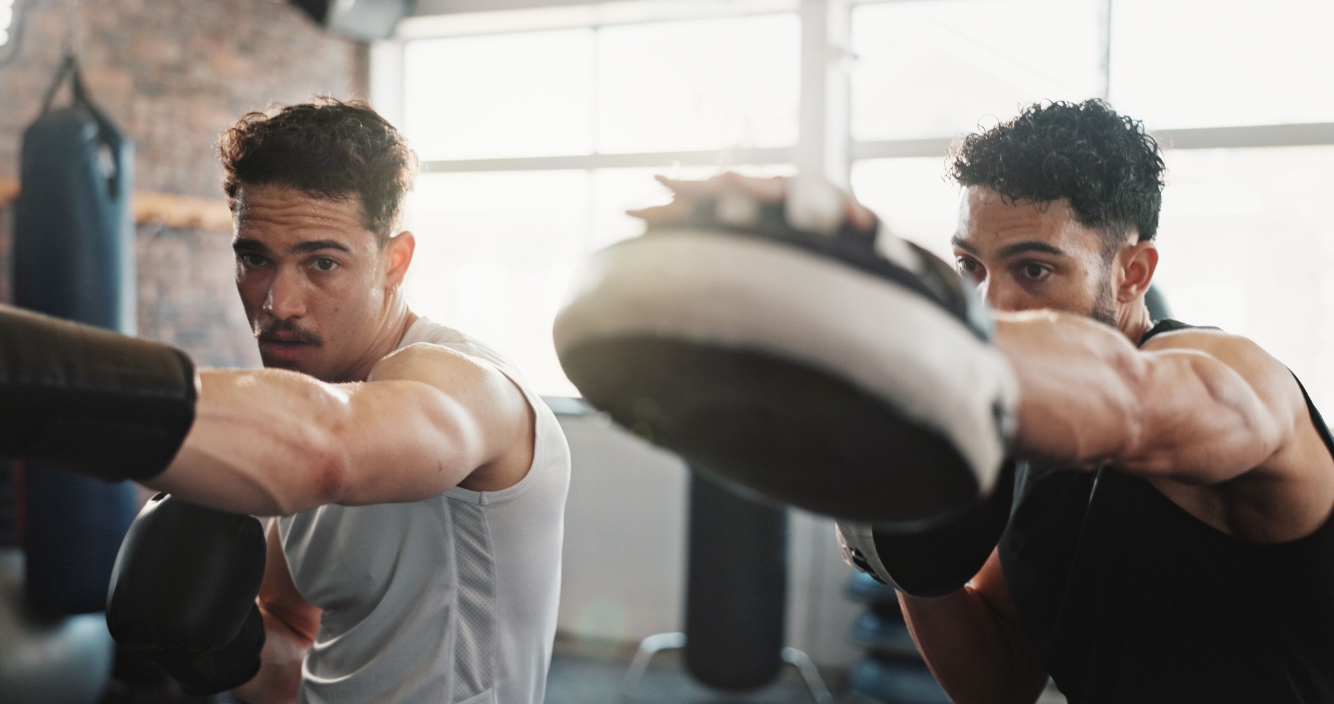 Männer, Personal Trainer oder Boxer mit Training im Fitnessstudio für gemeinsames Training, Exercise oder Workout. Männliche Person, Fitnesstrainer oder Trainer, die einem Kämpfer mit Handschuhen zur Selbstverteidigung im Fitnessstudio hilft
